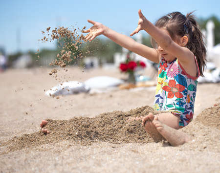 Little girl playing with sand on the beach. A cheerful child. The concept of summer vacation.の写真素材