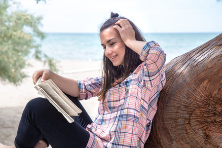 A happy girl reads a book on a tree, against the background of a sea beach. The person abstracted...