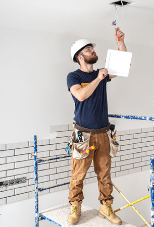 Electrician Builder at work, installation of lamps at height. Professional in overalls with an...