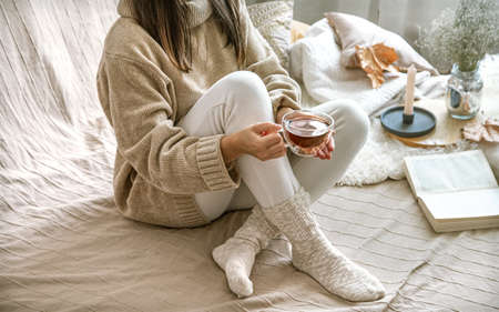 Cozy autumn or winter at home, a woman in a knitted sweater with a Cup of tea and a book.の写真素材