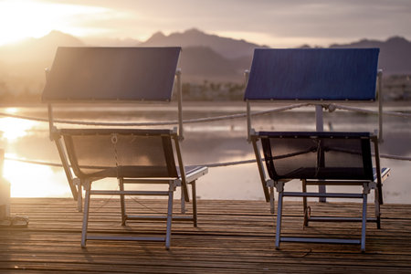 Two empty chairs on a wooden pier at sunset. Close up