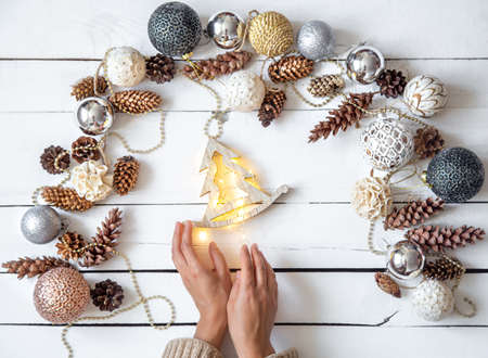 Composition with Christmas balls and women's hands. A woman holds a wooden toy with glowing lights. New year's holiday concept.の写真素材