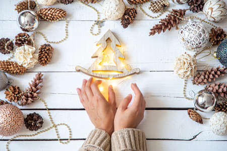 Composition with Christmas balls and women's hands. A woman holds a wooden toy with glowing lights. New year's holiday concept.の写真素材
