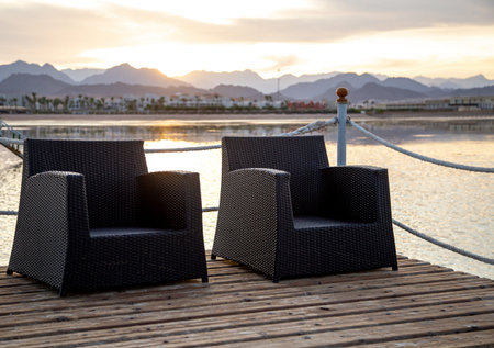 Two empty chairs on a wooden pier at sunset. Close up
