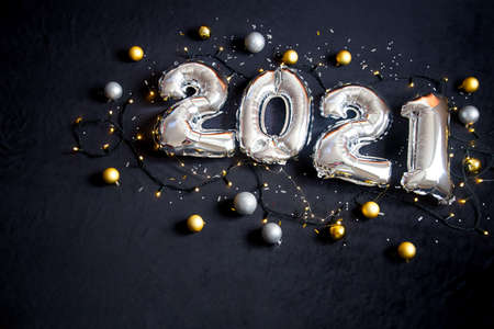 Silver foil balloons made numbers 2021 on black background with garland and balls. Holiday party decoration. Happy new year celebration, congratulation concept.の写真素材