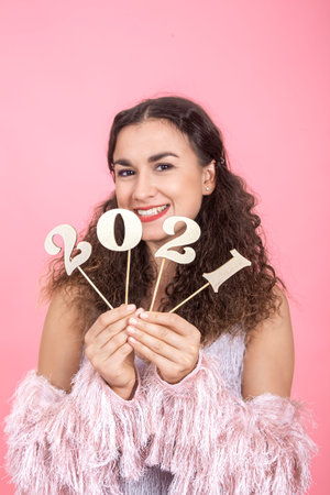 Elegant cheerful young brunette girl with curly hair and bare shoulders holds a wooden number 2021...