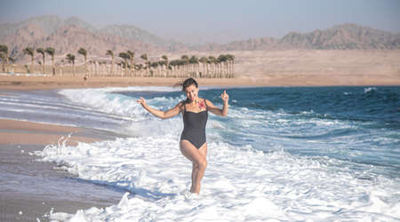 A cheerful woman in a black piecework swimsuit runs by the sea.の写真素材