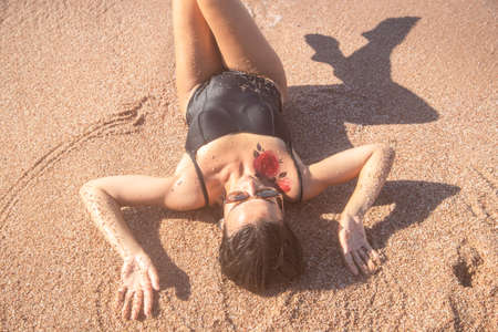 Beautiful woman in a black swimsuit lying on the sand by the sea, top view. The concept of relaxation and vacationの写真素材