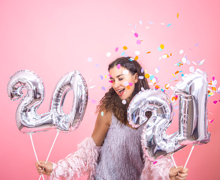 Beautiful young brunette girl with curly hair and festive clothes posing on a pink studio background...