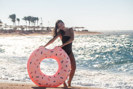 A cheerful woman with a donut-shaped swimming circle by the sea. The concept of leisure and...