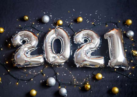 Silver foil balloons made numbers 2021 on black background with garland and balls. Holiday party decoration. Happy new year celebration, congratulation concept.の写真素材