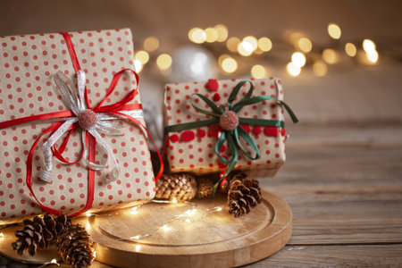 Christmas gifts packed in craft paper with ribbons, garland and decorative cones on blurred background.の写真素材