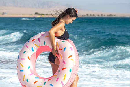 A cheerful woman with a donut-shaped swimming circle by the sea. The concept of leisure and entertainmentの写真素材