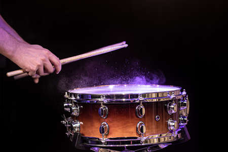 Drum sticks hitting snare drum with splashing water on black background under studio lighting close up.の写真素材