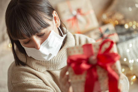 Young woman holding a beautifully wrapped christmas gift. Concept of celebrating christmas during coronavirus pandemic.の写真素材