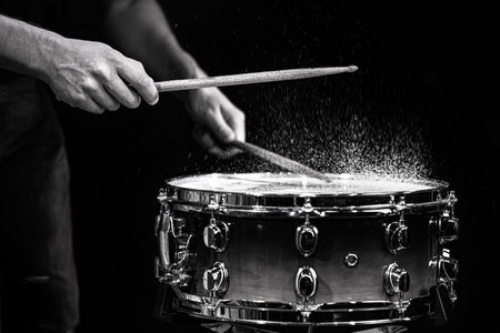 Drum sticks hitting snare drum with splashing water on black background under studio lighting. Black and white. Photo in motion.の写真素材