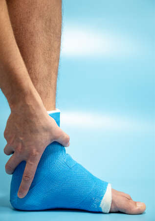 Blue splint ankle. Bandaged leg cast on male patient on light blue blurred background. Sports injury concept.の写真素材