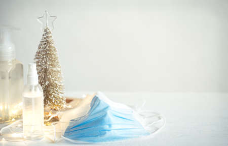 Hand sanitizer, disposable face masks, details of Christmas decor on blurred light background. Christmas and Coronavirus Pandemic concept. COVID-19.の写真素材