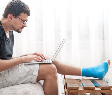 Young man with a broken leg in blue splint for treatment of injurie and ankle sprain is using a...