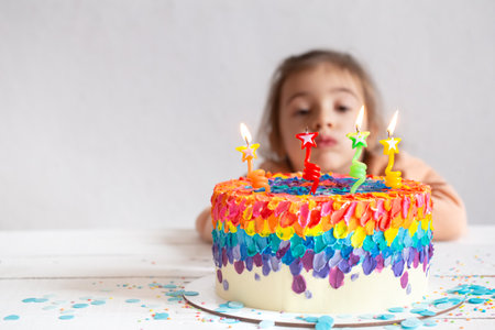 Multi-colored birthday cake decorated with cream and four candles. Birthday party concept.の写真素材