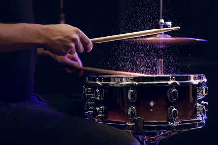 Drum sticks hitting snare drum with splashing water on black background under studio lighting close up.の写真素材