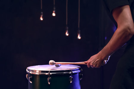 The percussionist plays with sticks on the floor tom in a dark room with beautiful lighting. Concert and performance concept.の写真素材