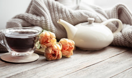 Festive home still life with flowers, a cup of tea and a teapot on a wooden surface close up.の写真素材