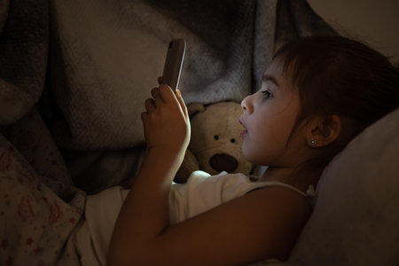 Little girl watching smartphone in bed, kid using phone and play game, child using mobile, addicted game and cartoon.の写真素材