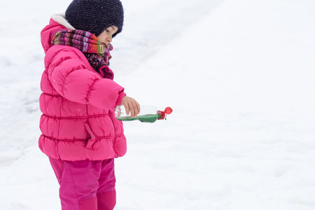 A cute girl with a bottle of paint draws on the snow. The concept of children's creativity and winter fun.の写真素材