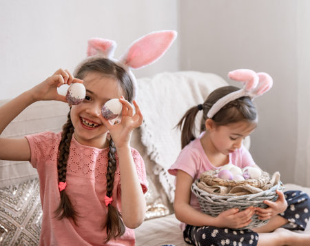 Little sisters with bunny ears posing for the camera with a basket of Easter eggs. Easter photo session concept.の写真素材