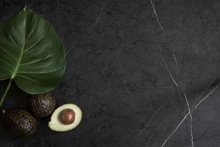 Still life with avocado fruits and natural leaves on dark marble copy space.の写真素材