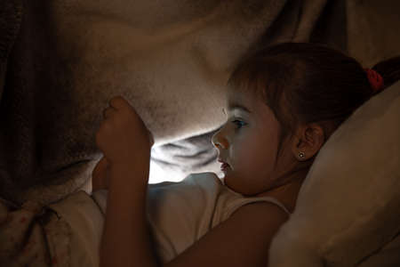 Little girl watching smartphone in bed, kid using phone and play game, child using mobile, addicted game and cartoon.の写真素材