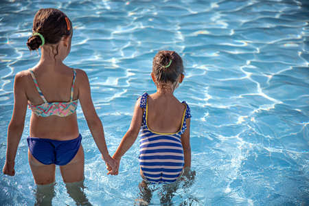 Cute little girls are holding hands while standing in the pool.の写真素材
