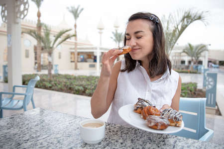 Cheerful young woman enjoying morning coffee with donuts on the outdoor terrace. Vacation and recreation concept.の写真素材