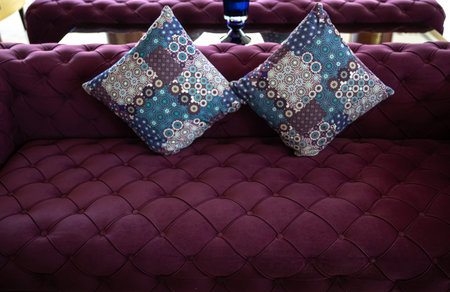 Purple velvet fabric modern sofa with sunken buttons and colorful decorative pillows. Idea and...