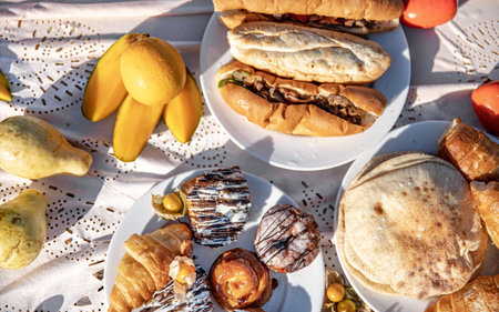 Hot dogs, croissants, tortillas and fruit on a breakfast tablecloth in the sunshine.