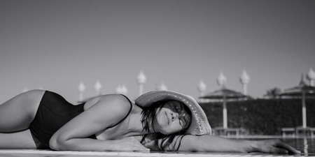 Attractive girl resting in the sun wearing a straw hat and a swimsuit. The concept of vacation in a...