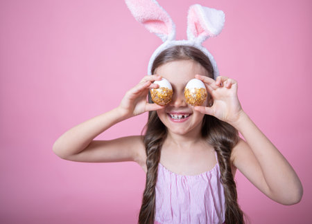 Little girl with easter bunny ears posing holding festive easter eggs in her hands on pink studio...