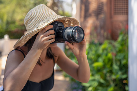 A young woman in a hat takes pictures with a professional SLR camera on a hot summer day.