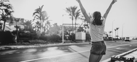 Black and white photo of a young girl in shorts in a jump in the summer near the roadway.の写真素材