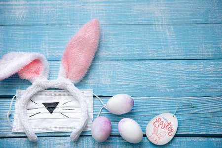 Easter still life with decorative Easter bunny ears, medical mask and eggs on a wooden surface. Easter holiday concept during a pandemic.の写真素材