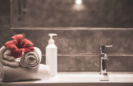 Spa composition with rolled clean towels, fresh flowers and a care product in a bottle with a dispenser on the washbasin in the bathroom.の写真素材