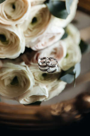 Wedding rings of the bride and groom on a mirror surface near fresh flowers. Celebration of the wedding and preparation.の写真素材