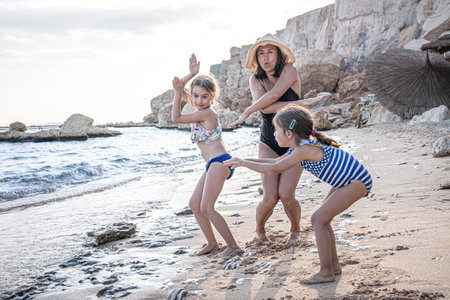 A young mother and two little daughters are having fun, dancing and laughing on the seashore. Happy family on vacation.の写真素材