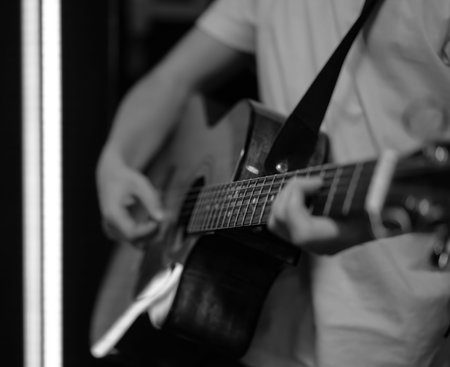 A man plays an acoustic guitar in a dark room. Live performance, acoustic concert, practice.