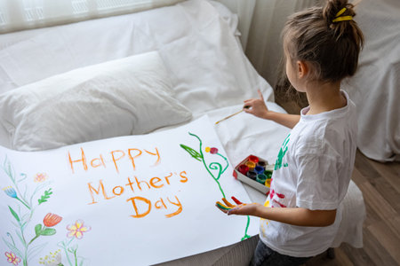 Little girl paints greeting card for Mom on Mother's Day with the inscription Happy mother's day and flowers.の写真素材