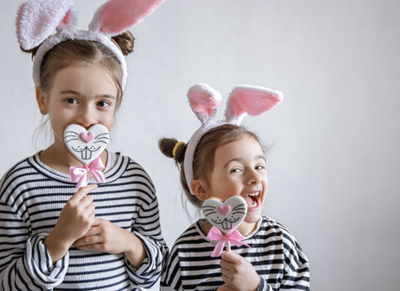 Funny little girls with Easter ears on their heads and Easter gingerbread on sticks.