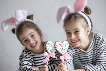 Little girls with Easter bunny ears on their heads are holding gingerbread cookies on sticks.