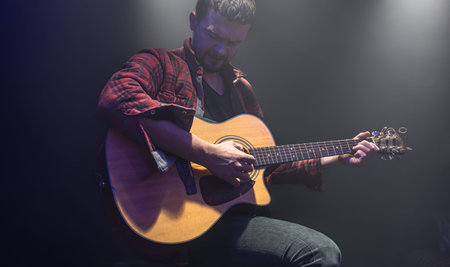 A man plays an acoustic guitar at a partially lit concert.