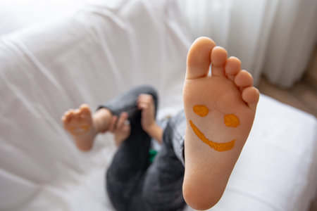 A little girl is lying on a sofa with her feet painted with paints. Funny smiles on children's feet.